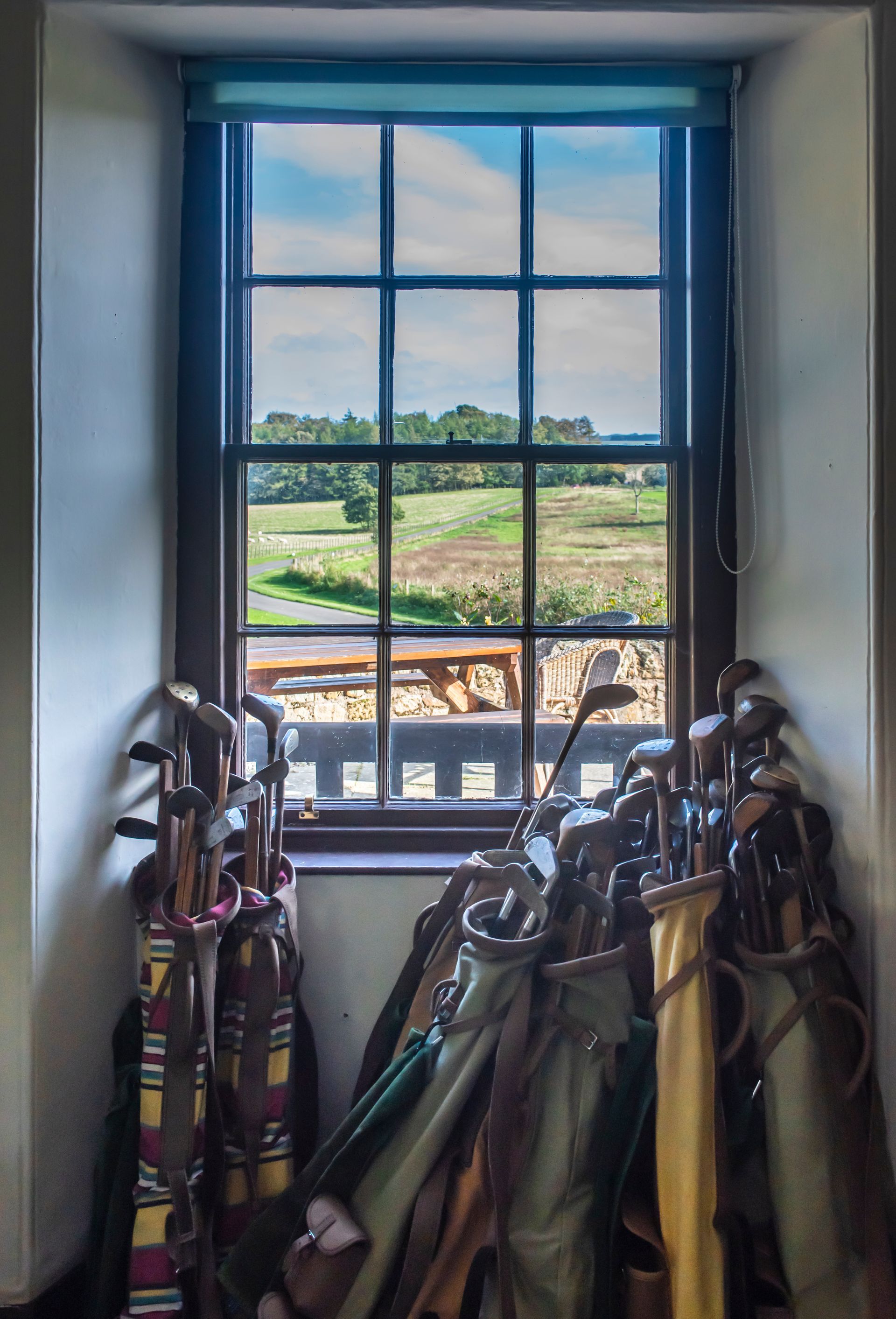 Golf clubs in bags by a window overlooking a green field.