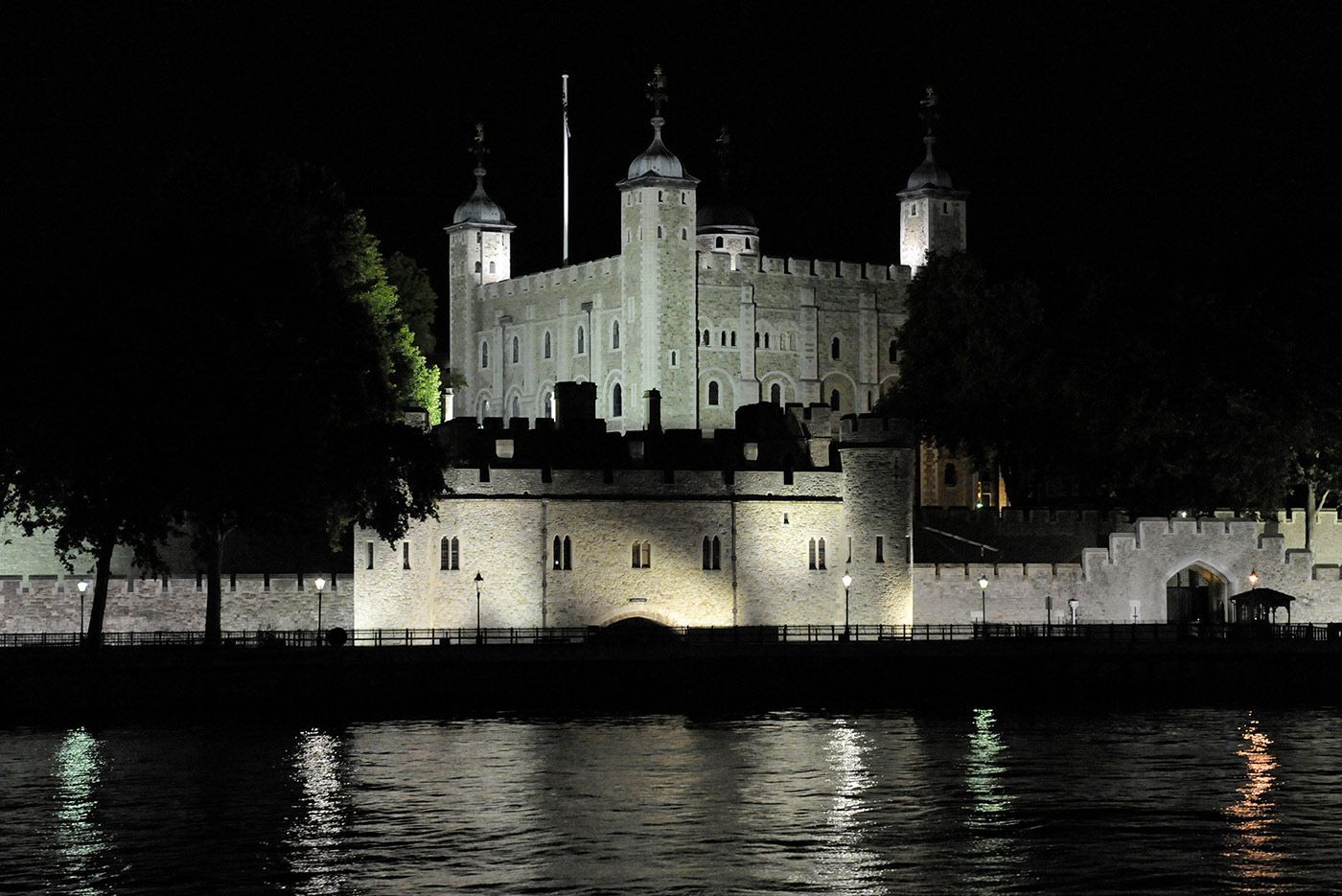 Tower of London illuminated at night, reflected in the water.