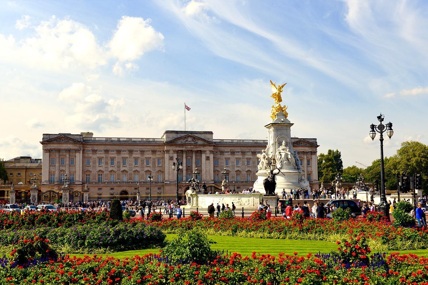 Buckingham Palace, London, with the Victoria Memorial in front; blue sky, sunny day, many people.
