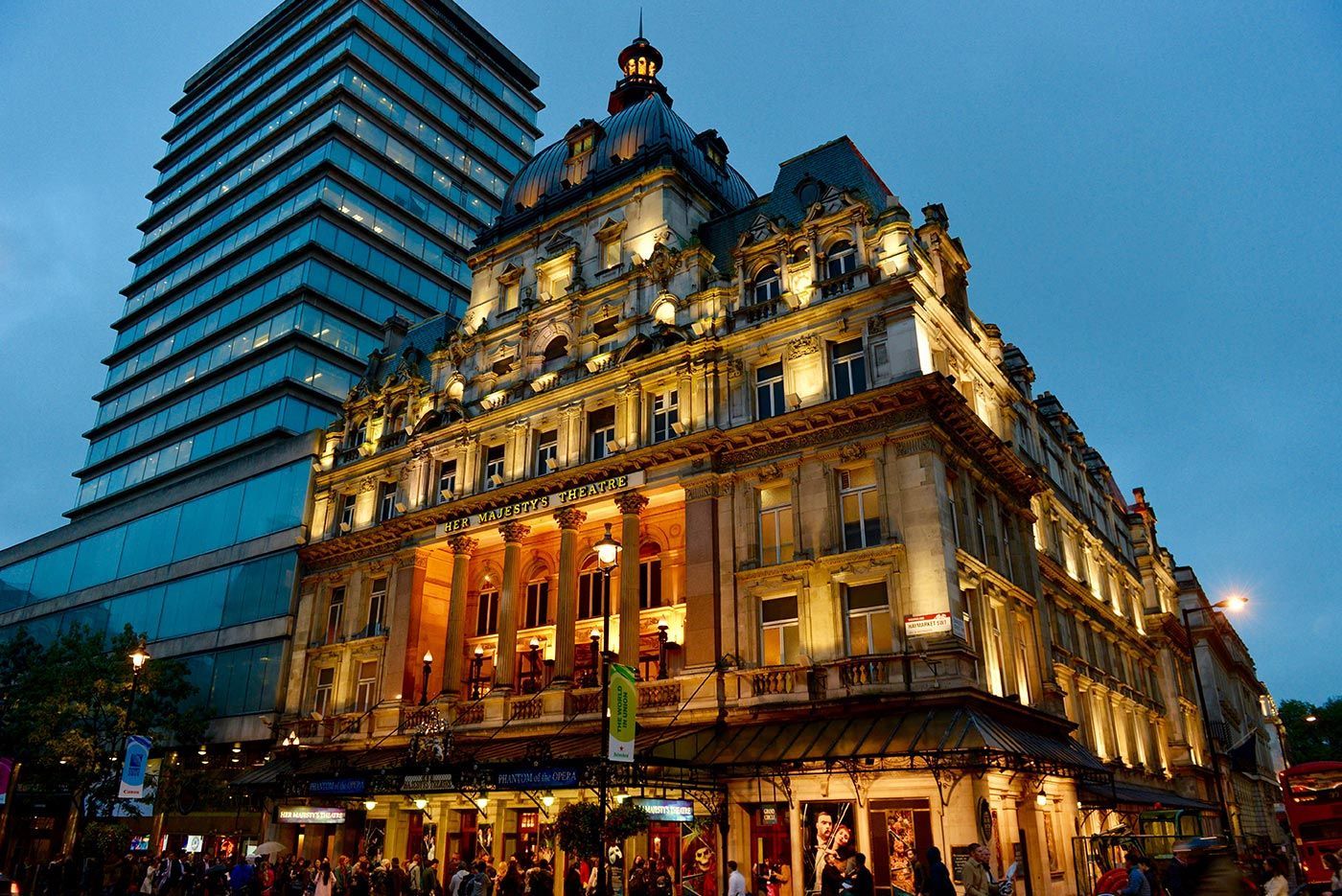 Historic building illuminated at dusk, with ornate facade and modern skyscraper alongside.