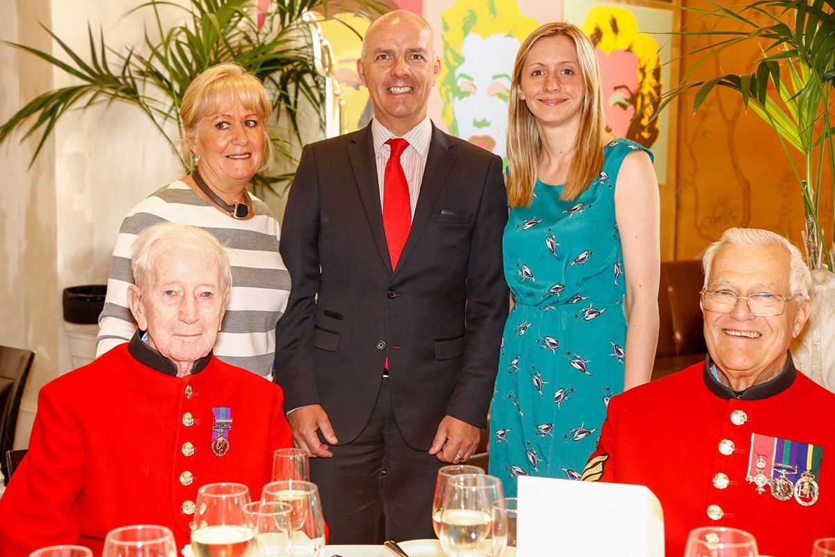 People in a restaurant pose with two men in red uniforms, celebratory event.