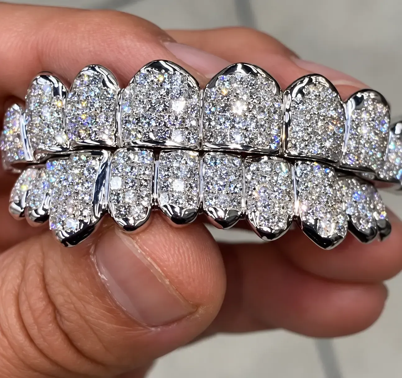 Close-up of diamond-encrusted silver grillz with sparkling stones on upper and lower teeth, held by hand.