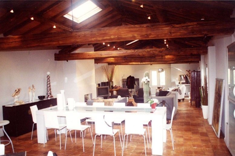 Ampia camera con tavolo e sedie bianchi, travi in ​​legno a vista e lucernario.