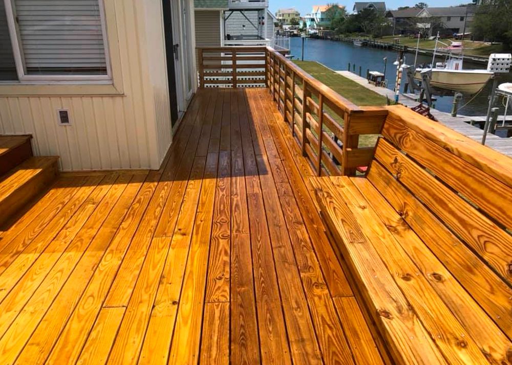 Wooden deck with railing and built-in seating, overlooking a canal.
