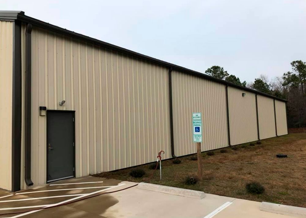 Tan metal-sided building with a black door and brown trim; accessible parking sign in front.