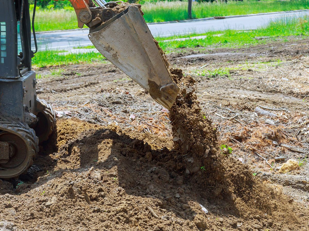 Mini excavator, its bucket pouring dirt onto a construction site.