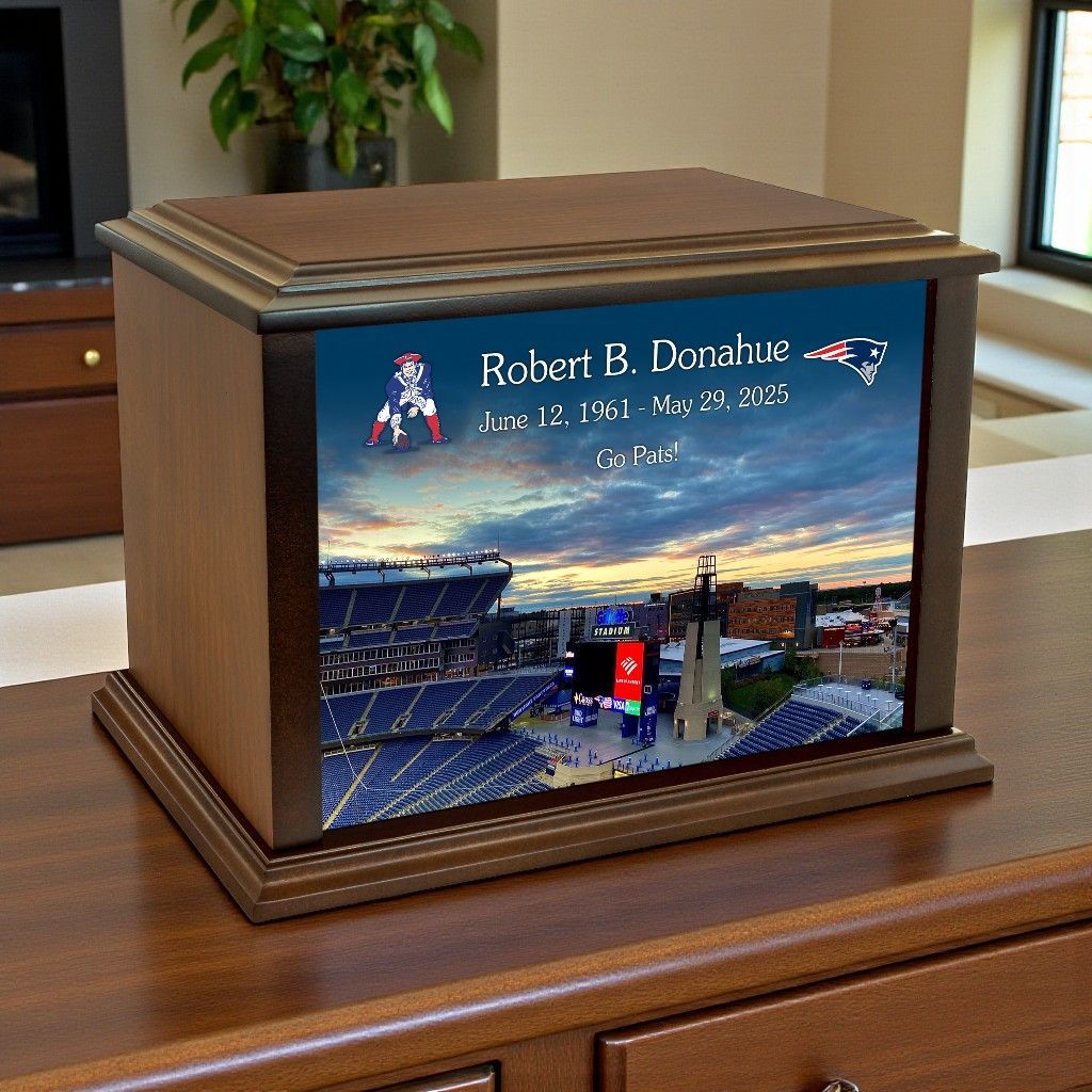 A wooden cremation urn featuring a New England Patriots themed graphic of a stadium at sunset and memorial text.