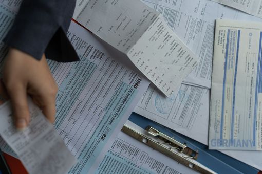 Hand sorting papers and forms spread across a desk with a pen and calculator nearby