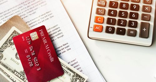 Red credit card and dollar bills beside a calculator on paper documents