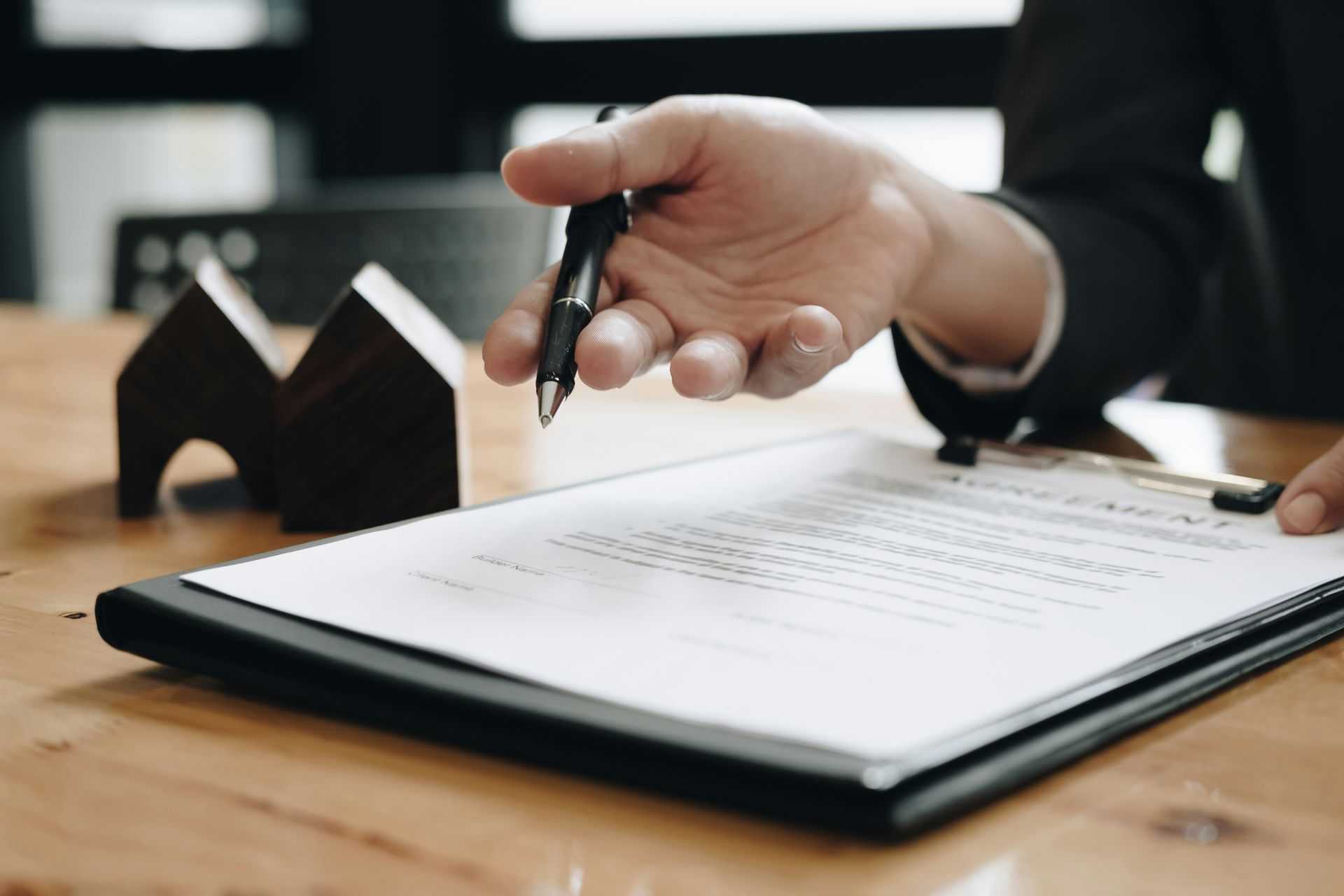 Hand holding a pen over a signed document on a wooden table, with a small desk clock in the background