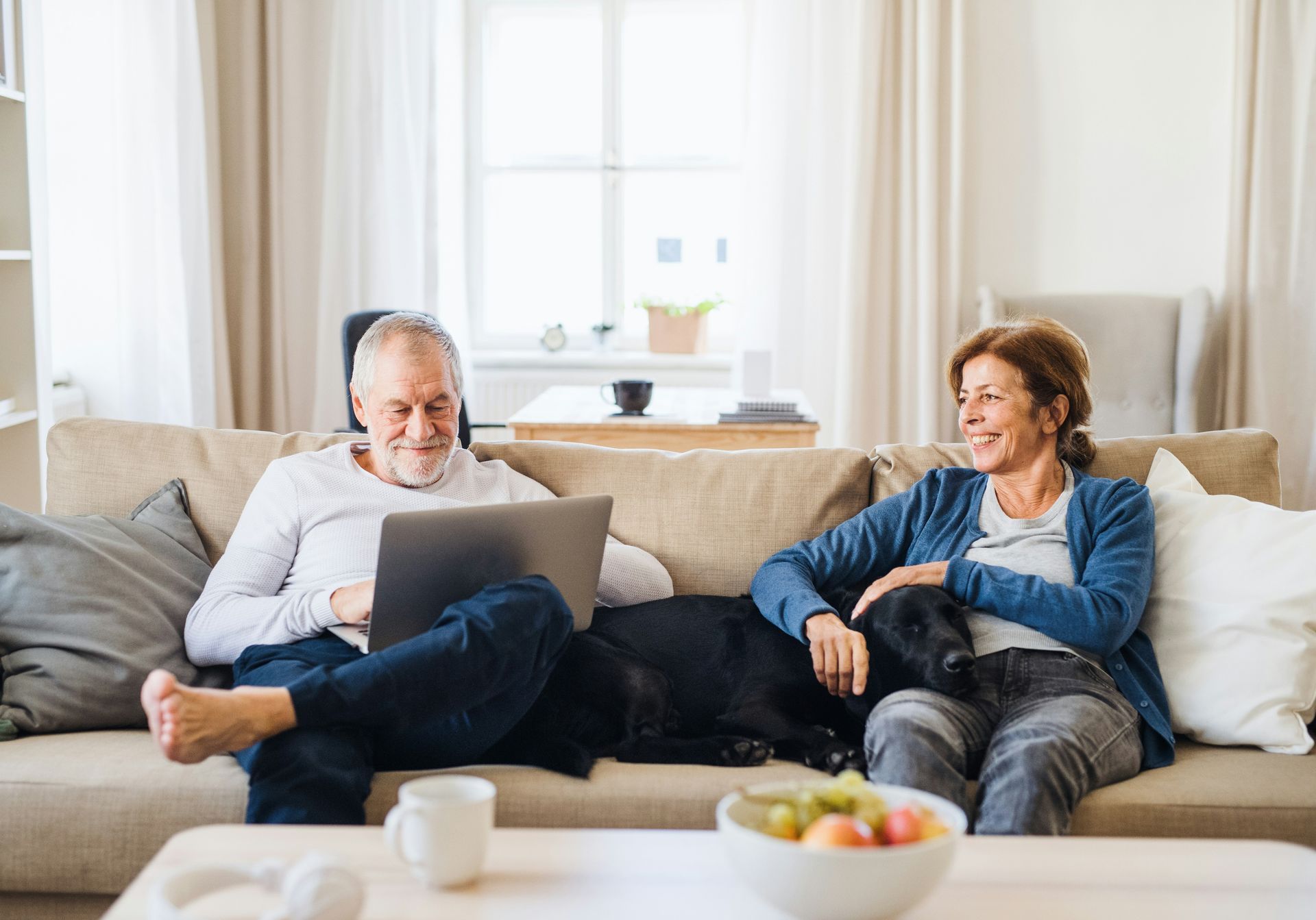 Two people relaxing on a couch with a laptop in a bright living room