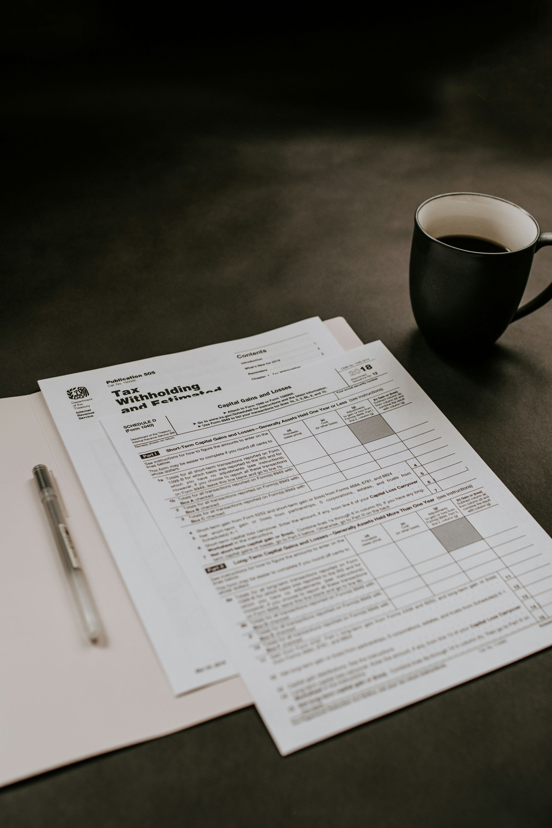 Papers, pen, and coffee cup on a desk in a dimly lit workspace