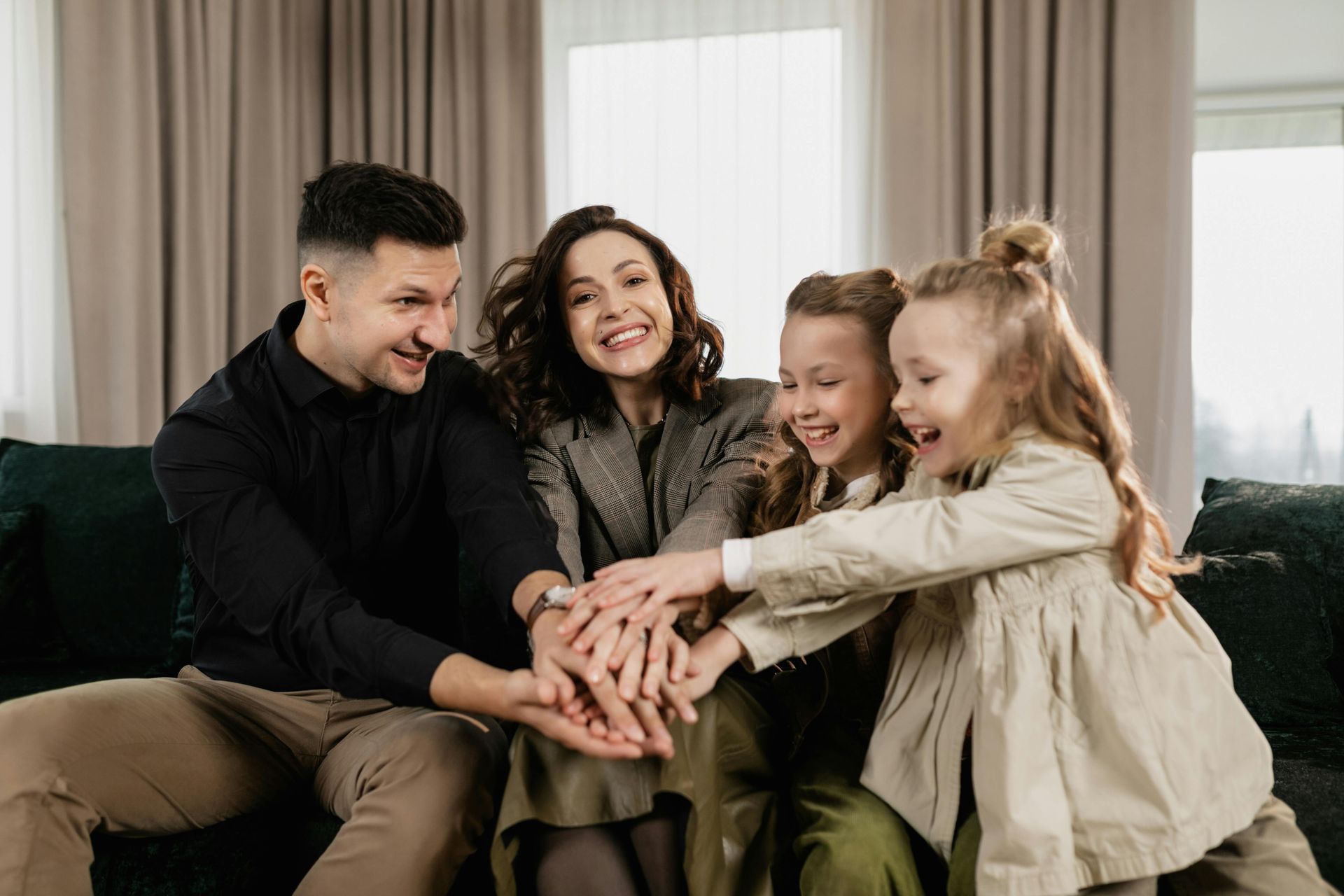 Four smiling people on a couch stack their hands together in a cozy living room
