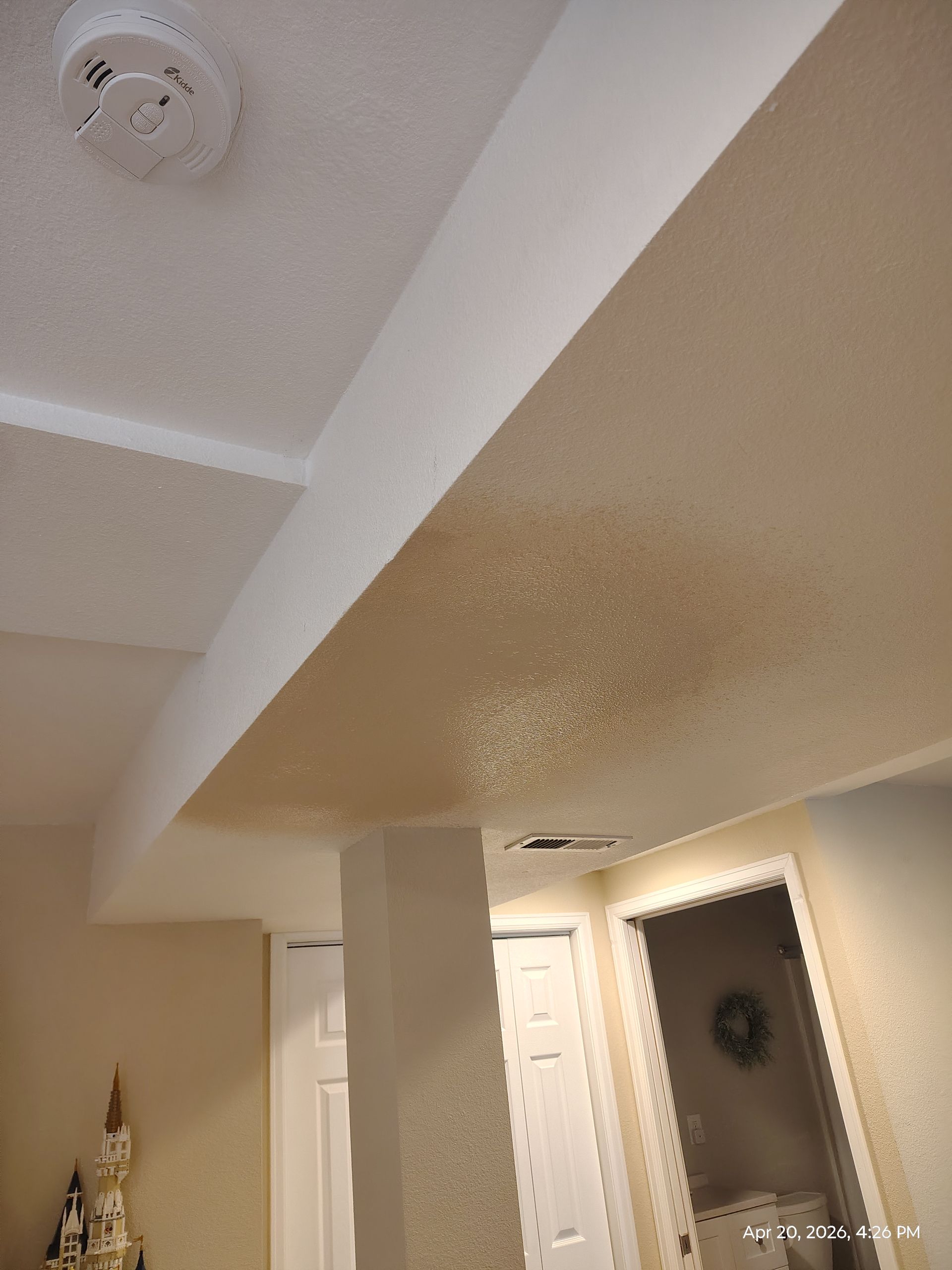 Indoor hallway ceiling with beige walls, white trim, and a smoke detector near a doorway.