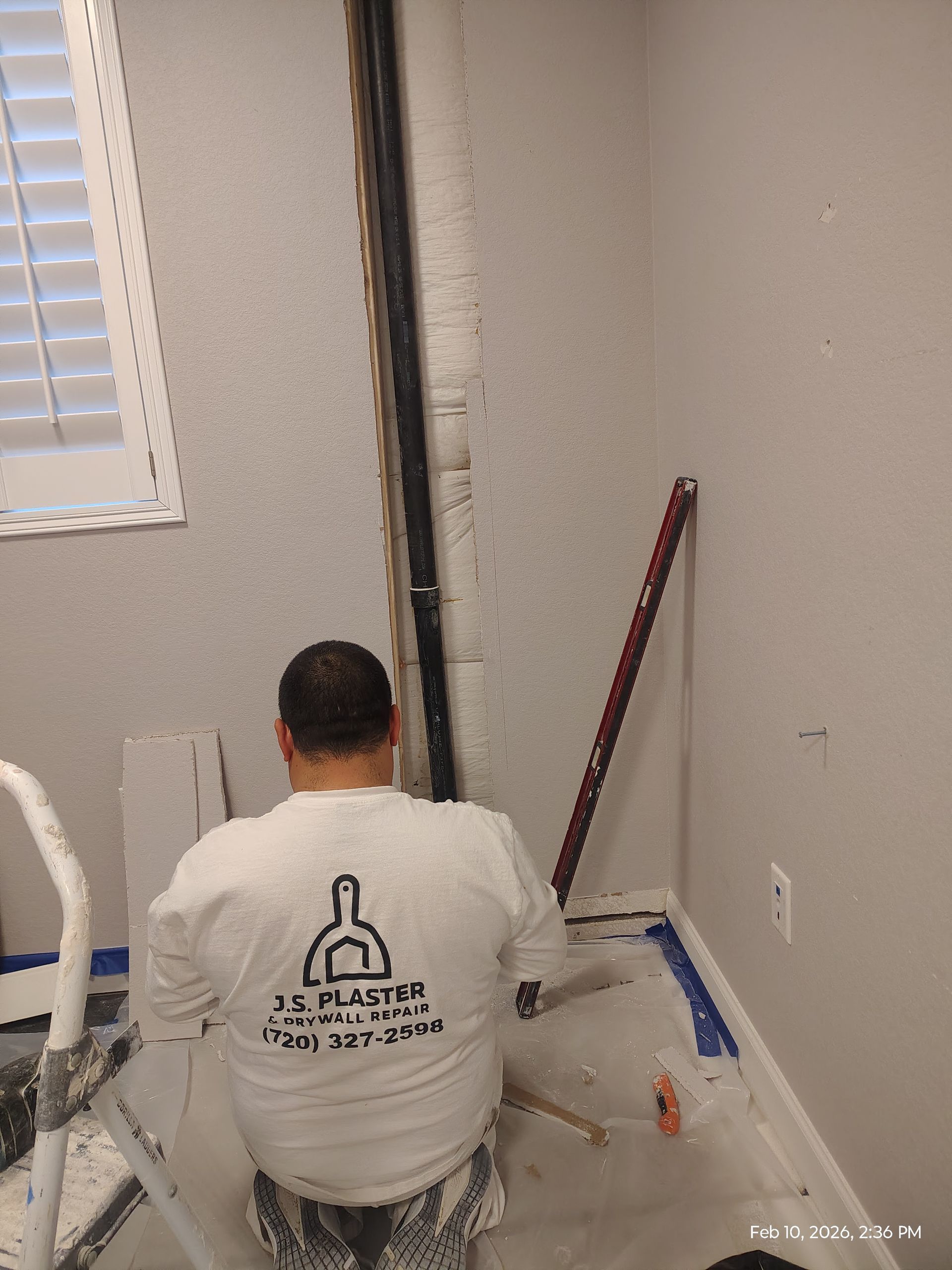 Worker kneeling on floor near wall, using tools in a room under renovation.