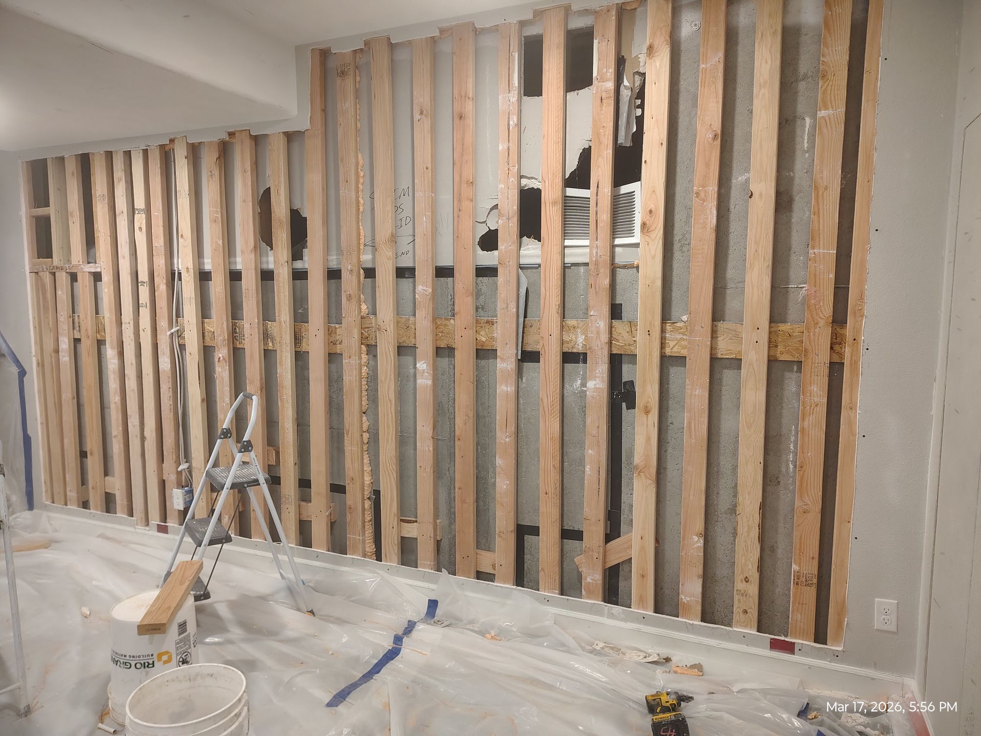 Indoor renovation with exposed wall studs, a step ladder, and a plastic-covered floor