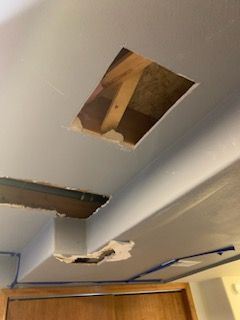 Ceiling with two holes exposing wood beams and damaged drywall near a wall