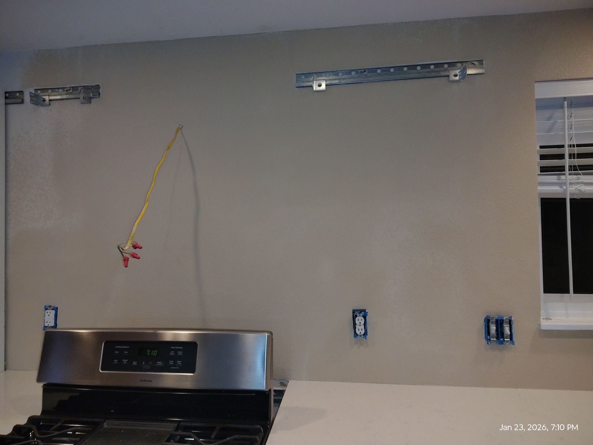 Empty kitchen wall above stove with a yellow hanging cord and a window on the right.