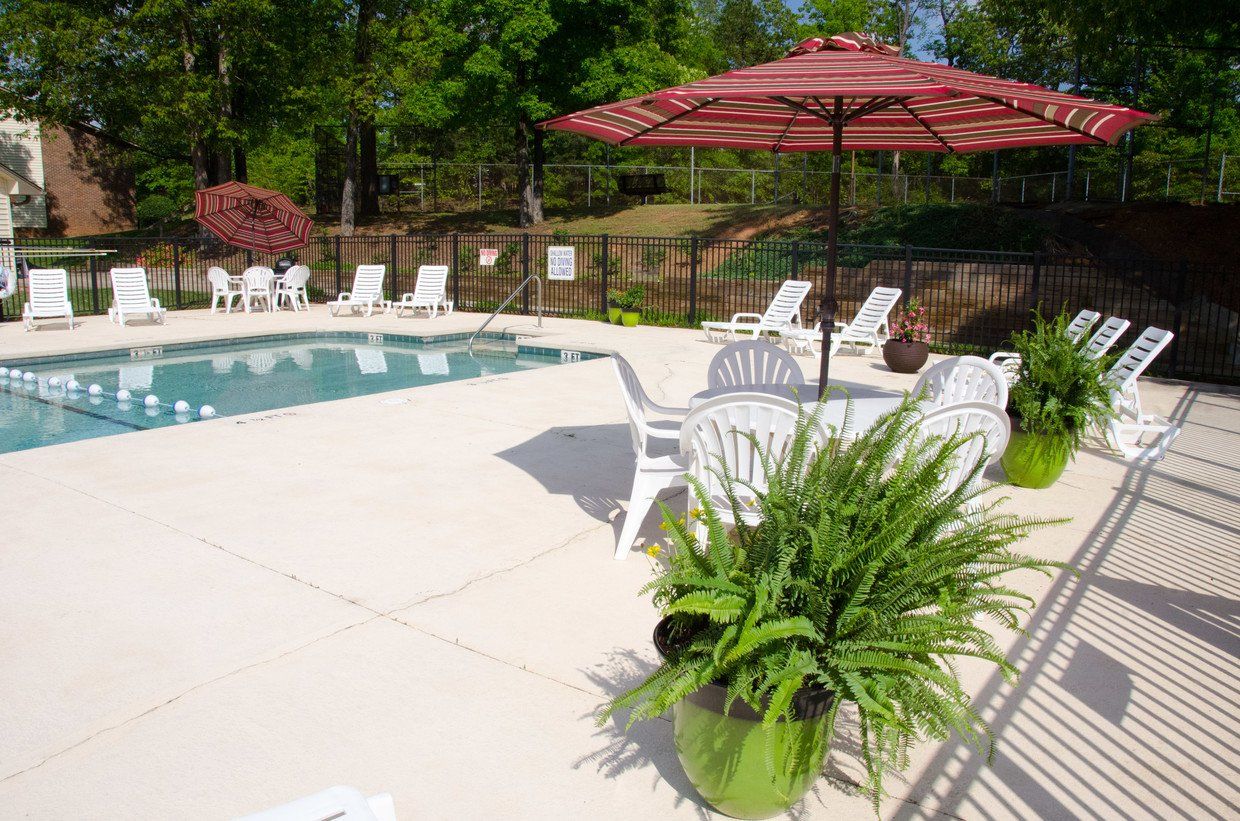 View of pool with chairs and red umbrella.