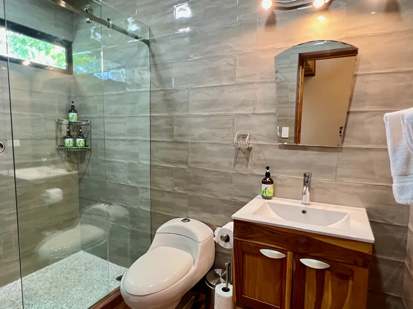A bathroom with a toilet , sink , mirror and walk in shower.