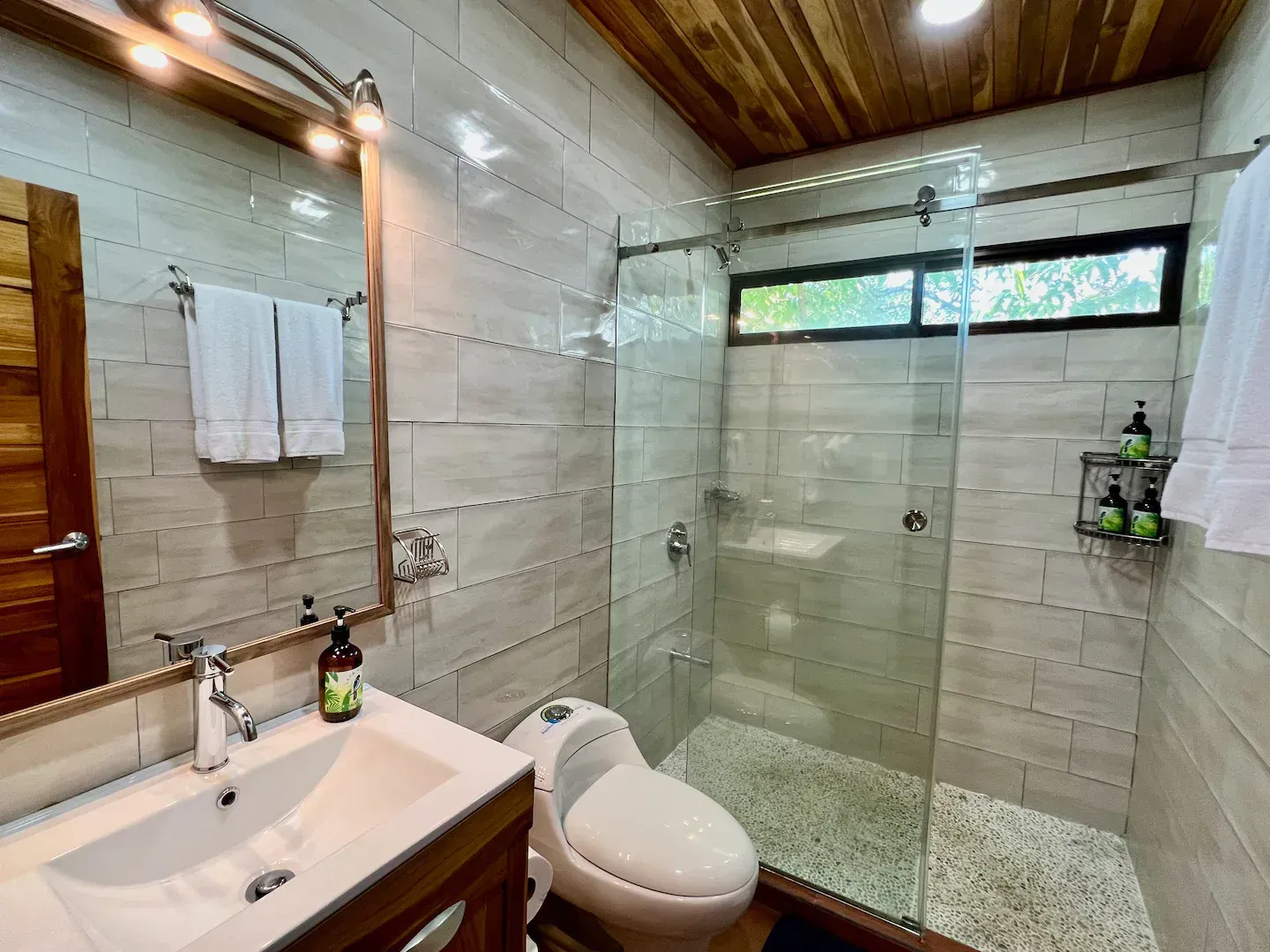 A bathroom with a toilet , sink , mirror and walk in shower.