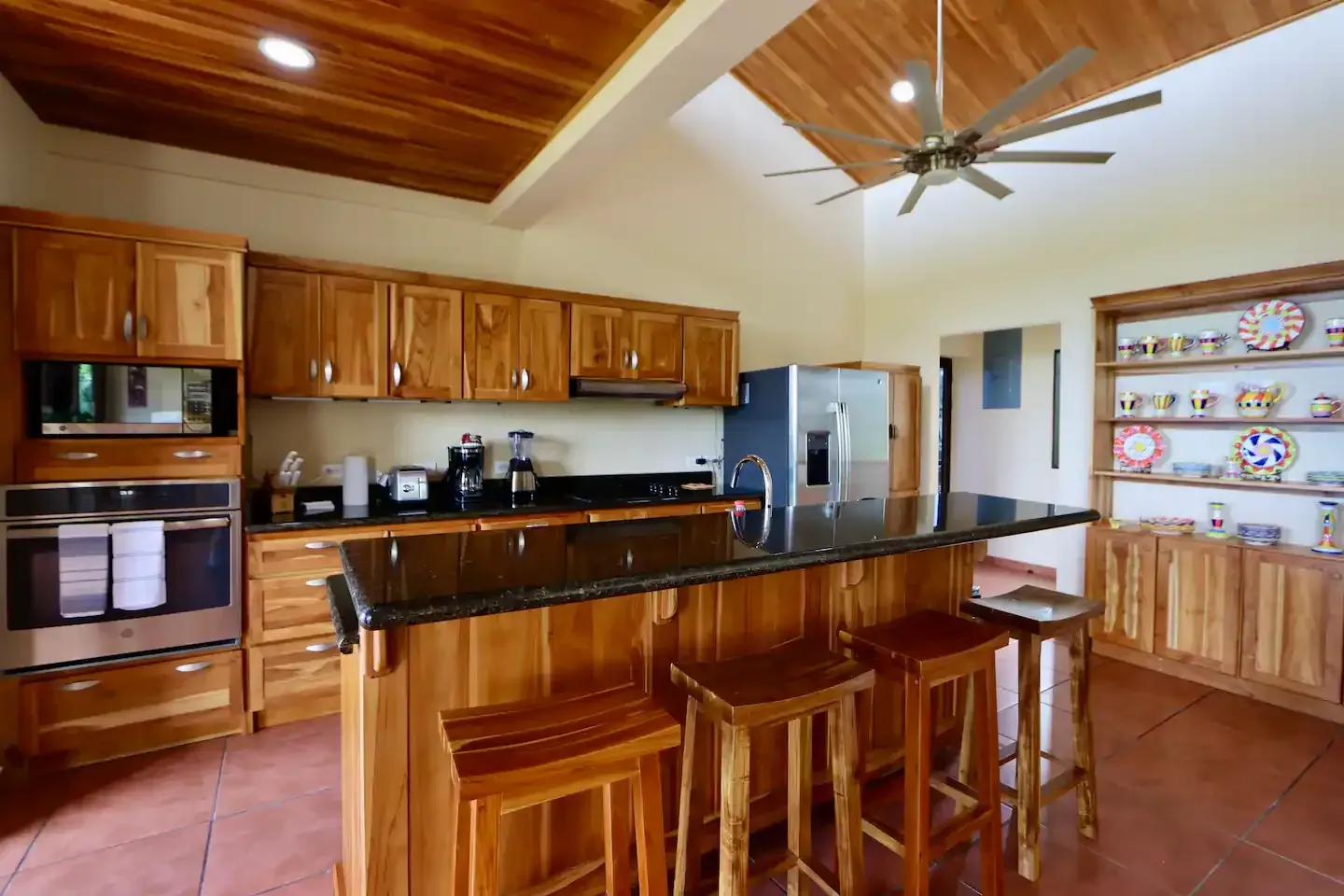 A kitchen with wooden cabinets and stools and a ceiling fan