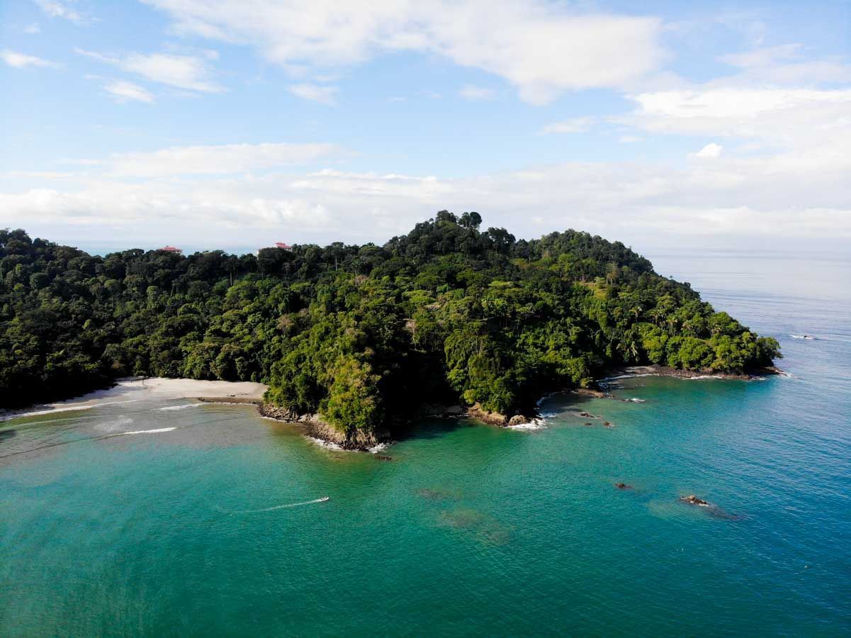An aerial view of a small island in the middle of the ocean surrounded by trees.