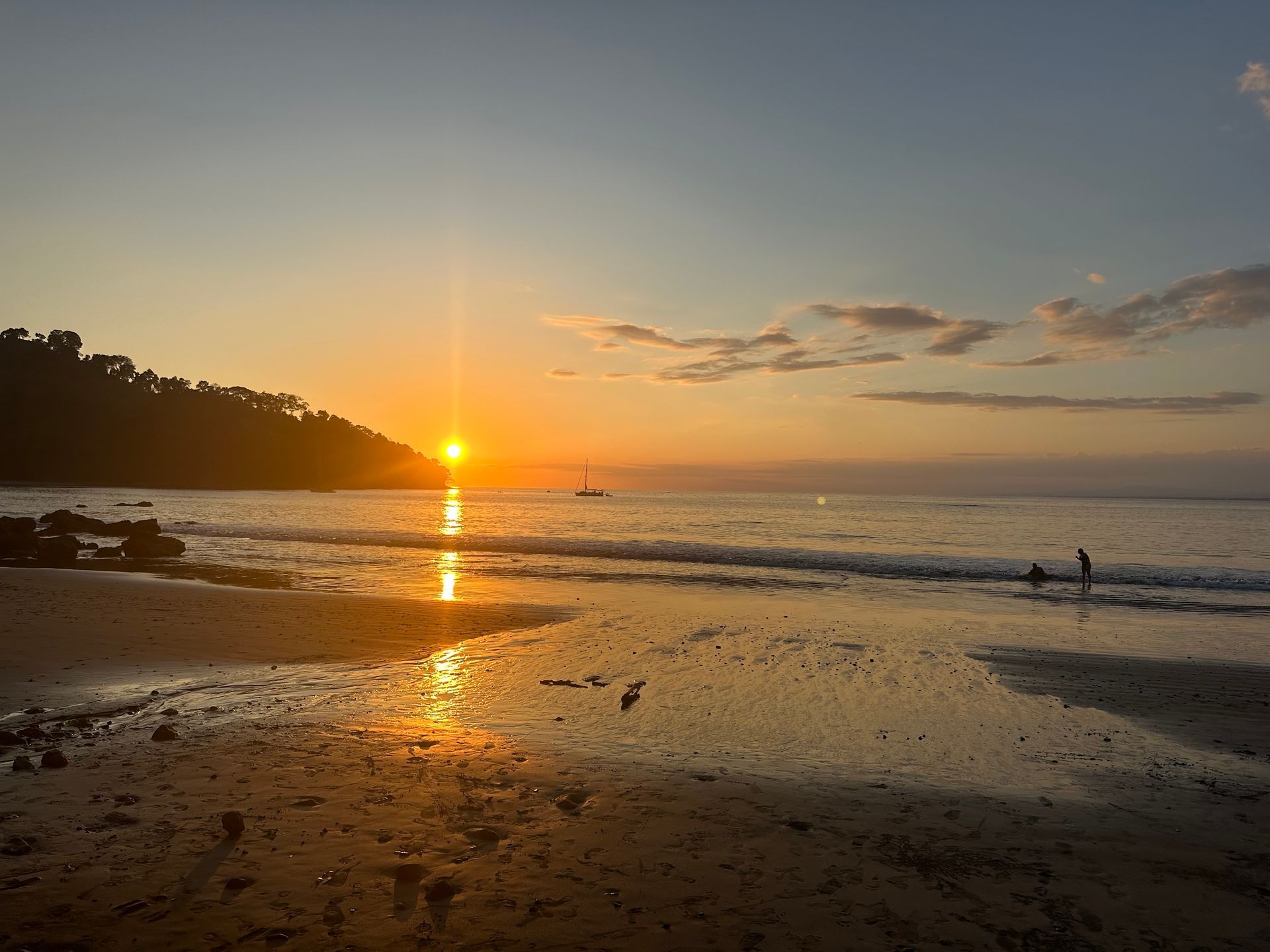 The sun is setting over the ocean and a person is walking on the beach.