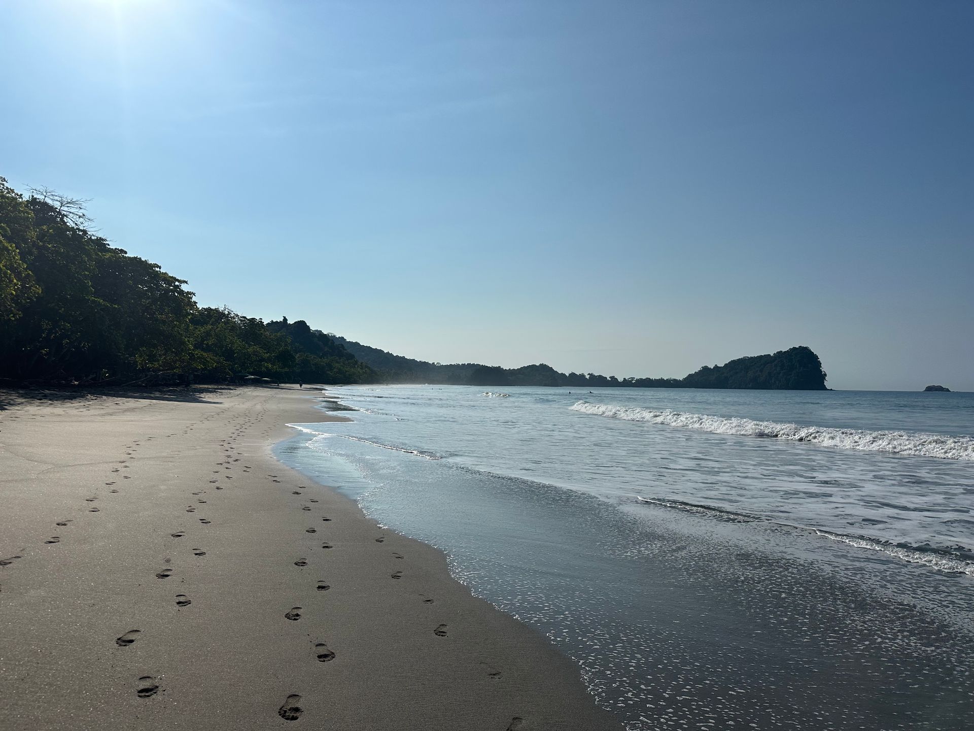 A beach with footprints in the sand and waves coming in
