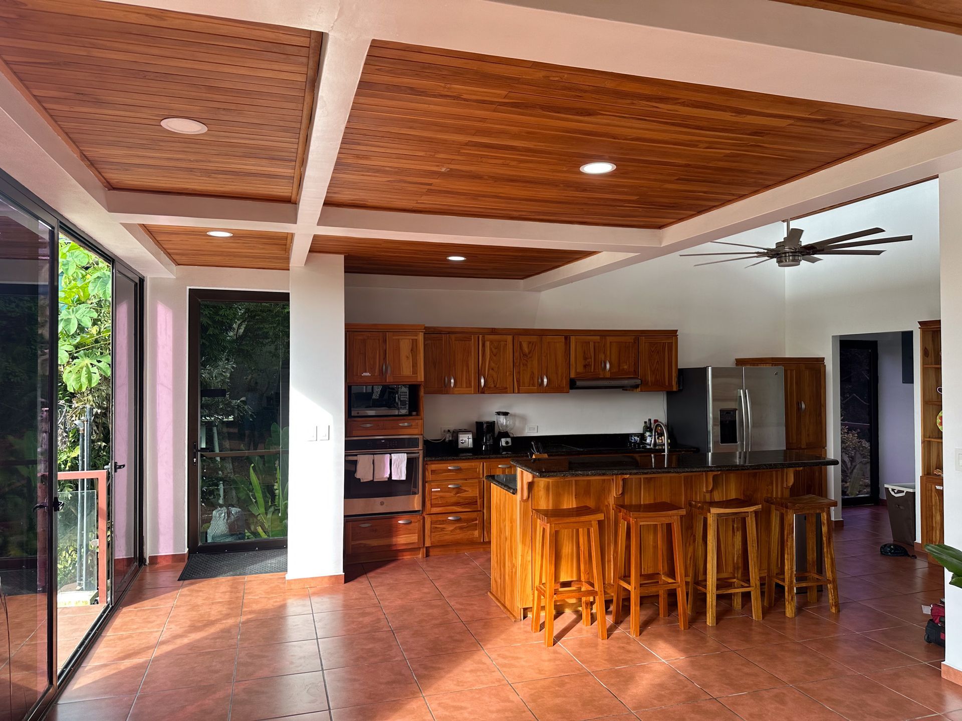 A kitchen with wooden cabinets and stools and a ceiling fan