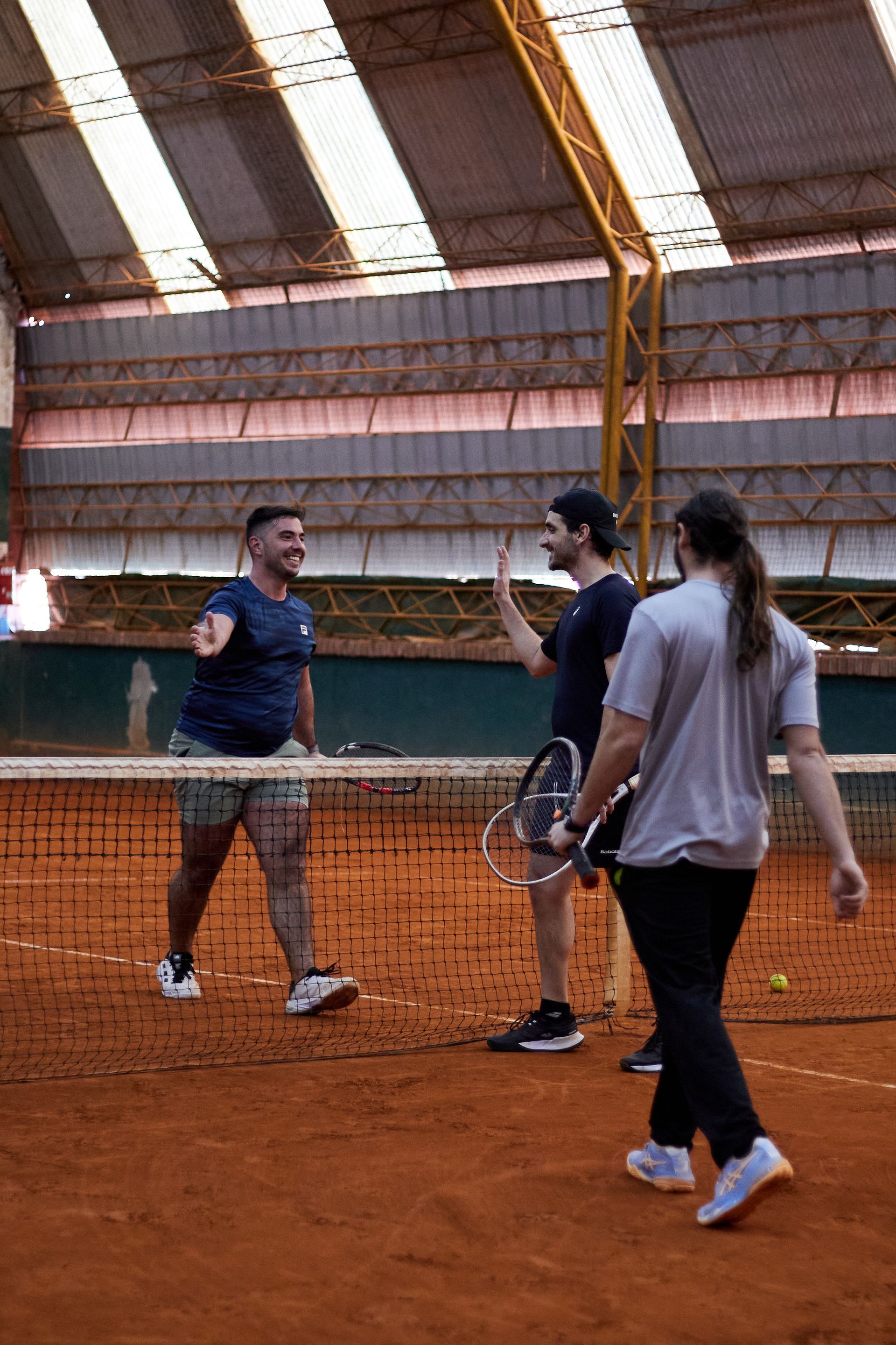 Tres personas conversando en una cancha de tenis cubierta de tierra batida, cerca de la red.