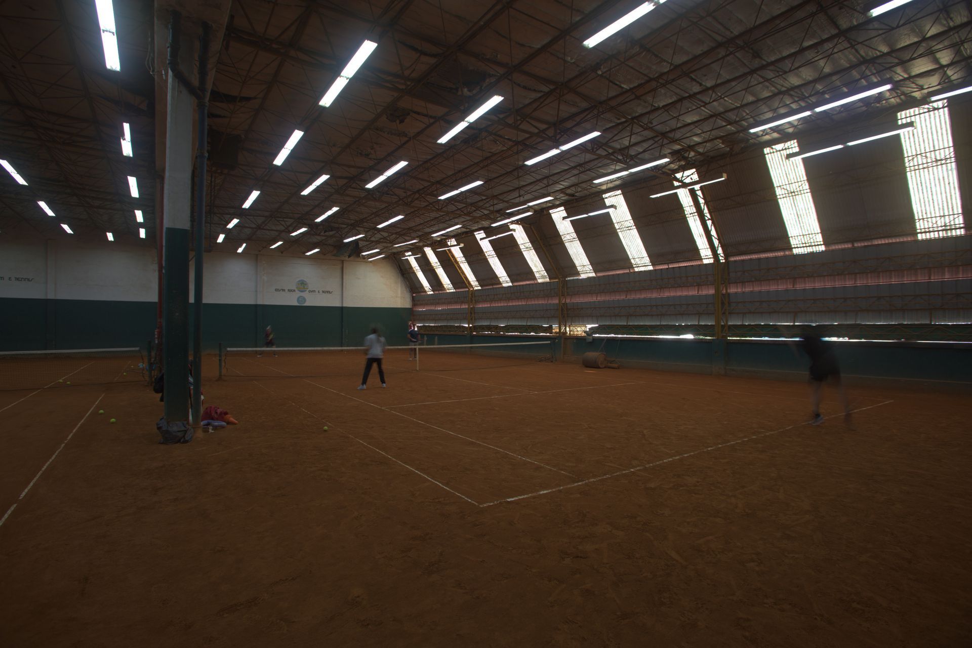 Tres personas conversando en una cancha de tenis cubierta de tierra batida, cerca de la red.