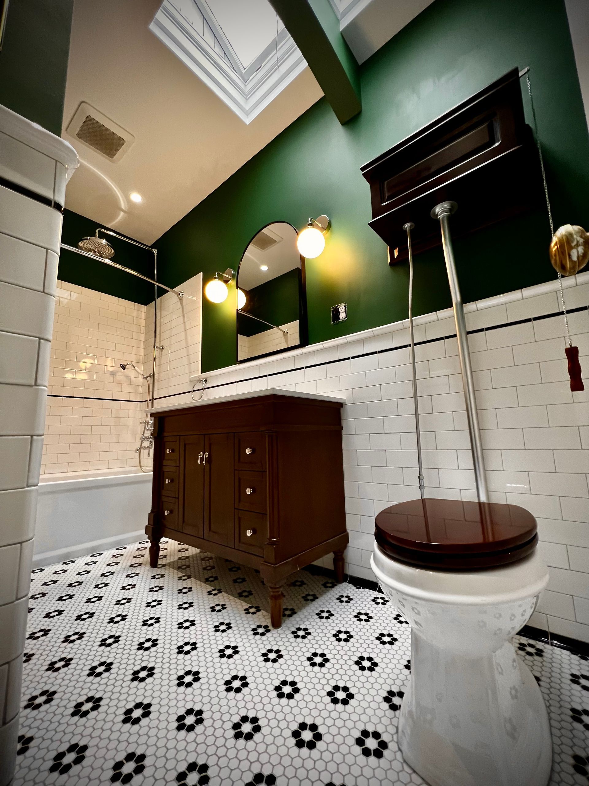Modern bathroom with white tile, dark green walls, skylight, vanity, and toilet-paper holder
