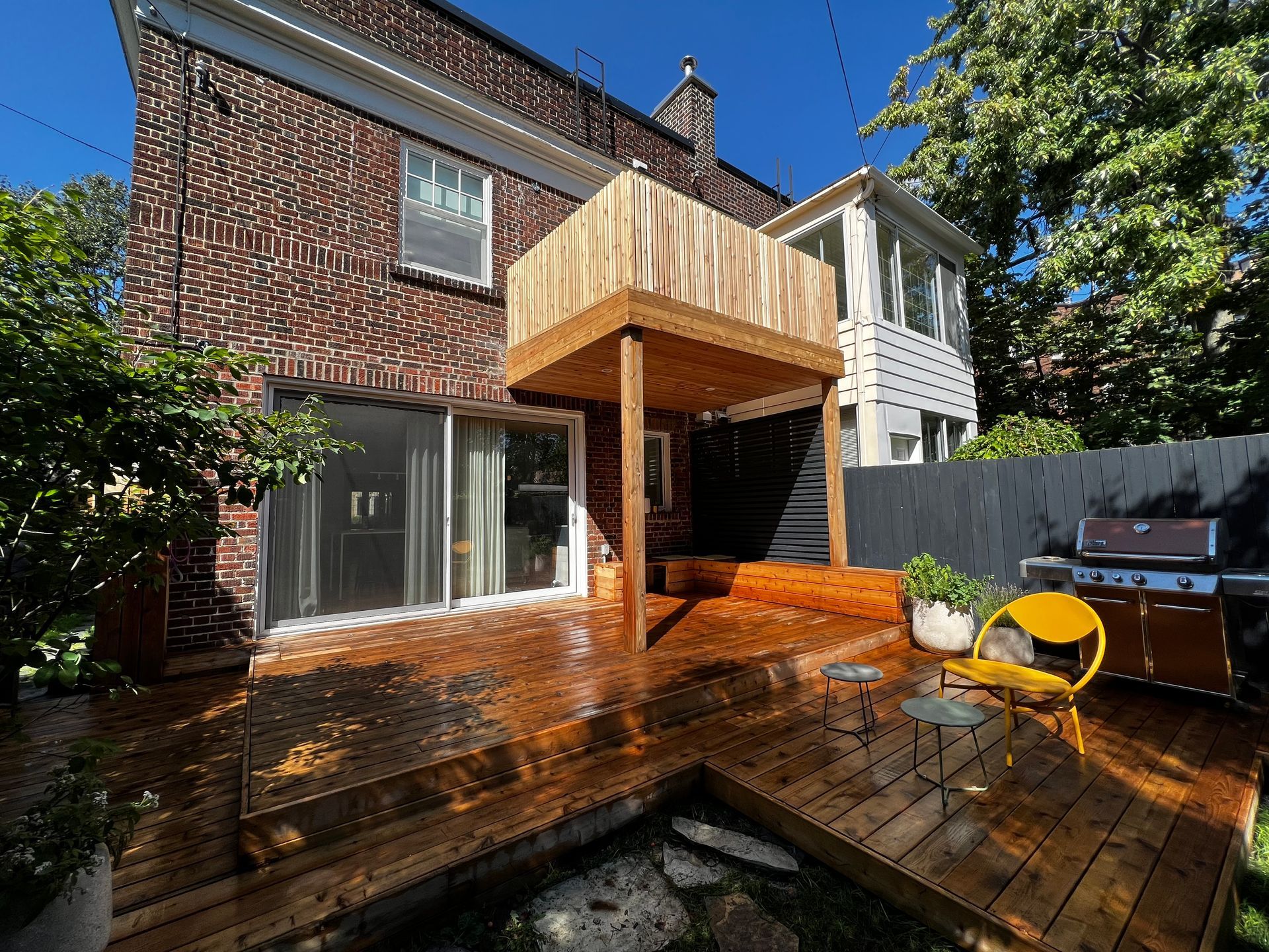 Wooden backyard deck with a covered patio, gray siding, and two yellow chairs beside a house