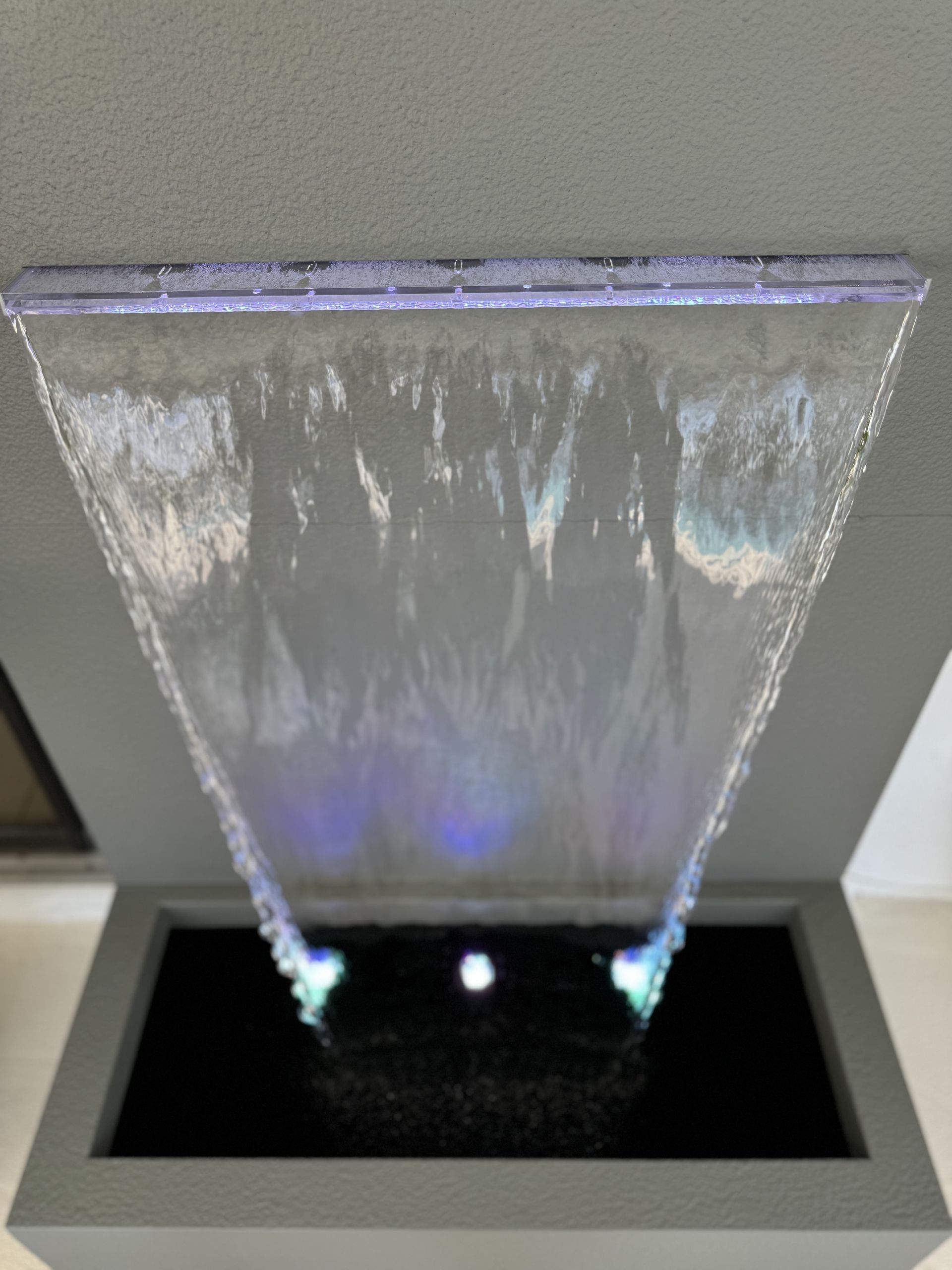 Water fountain with water cascading into a dark basin, illuminated with blue and green lights