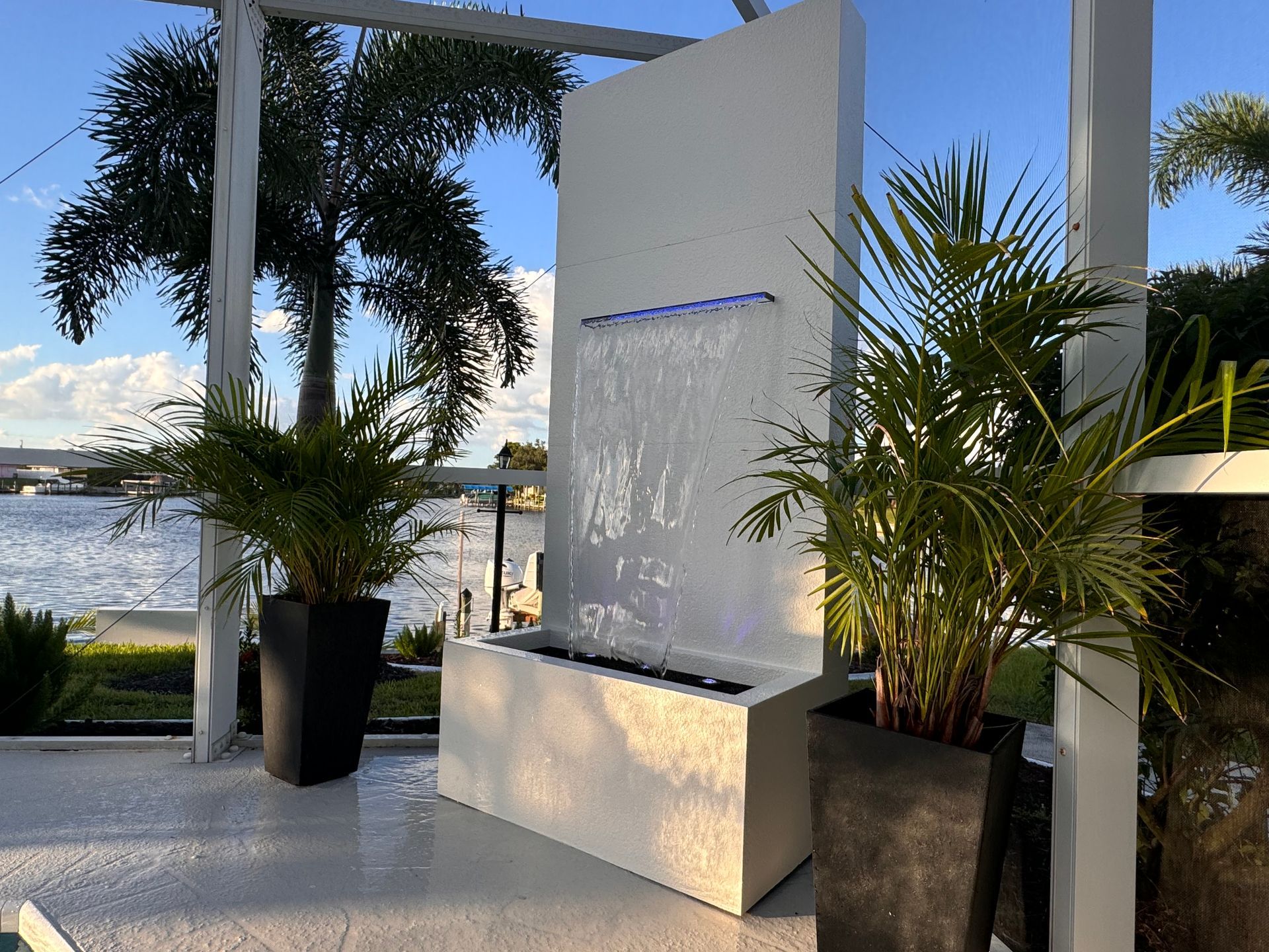 Modern white water fountain with plants, set outdoors near a waterway