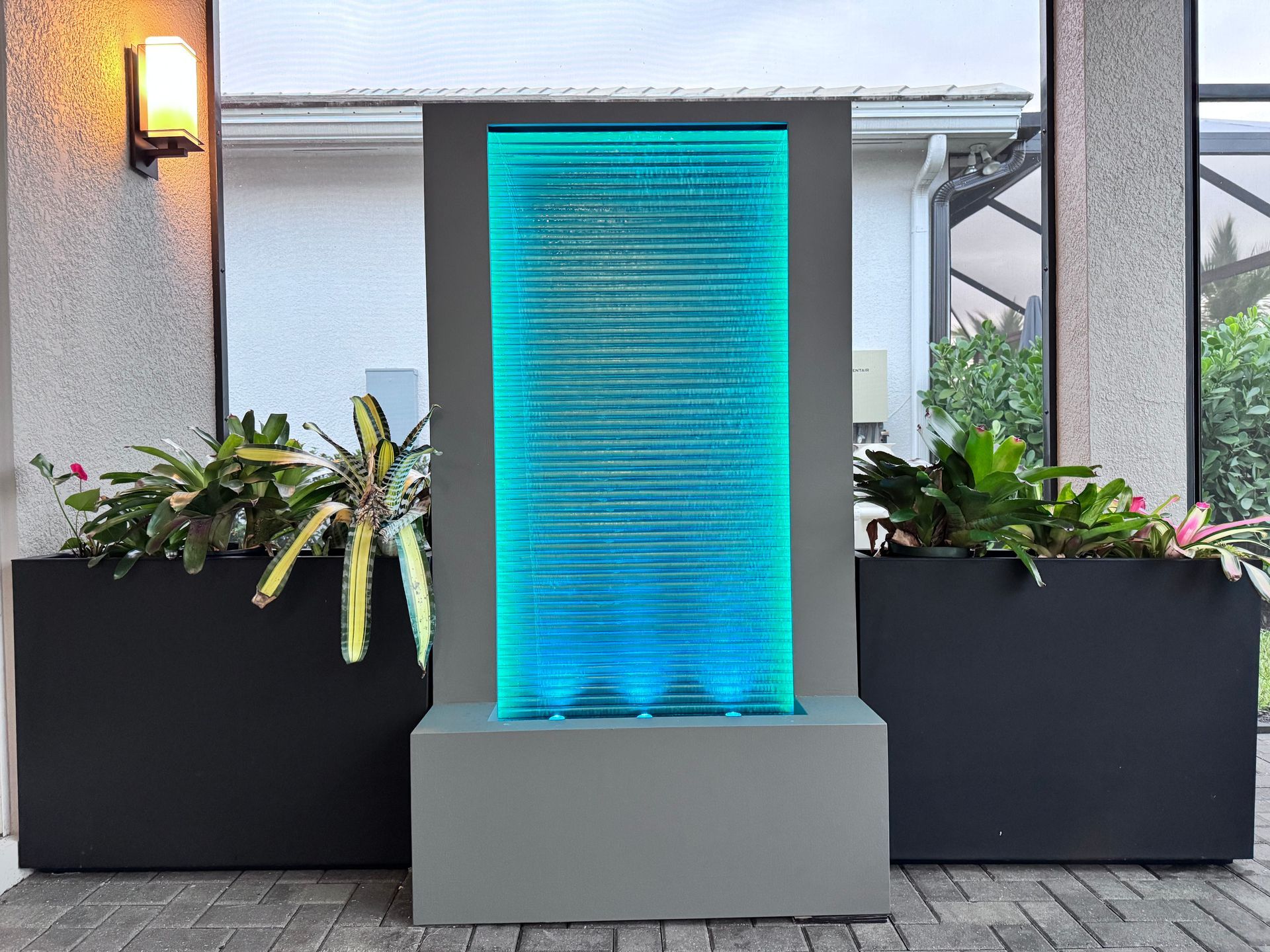 Modern outdoor water fountain with blue LED lights, between two planters