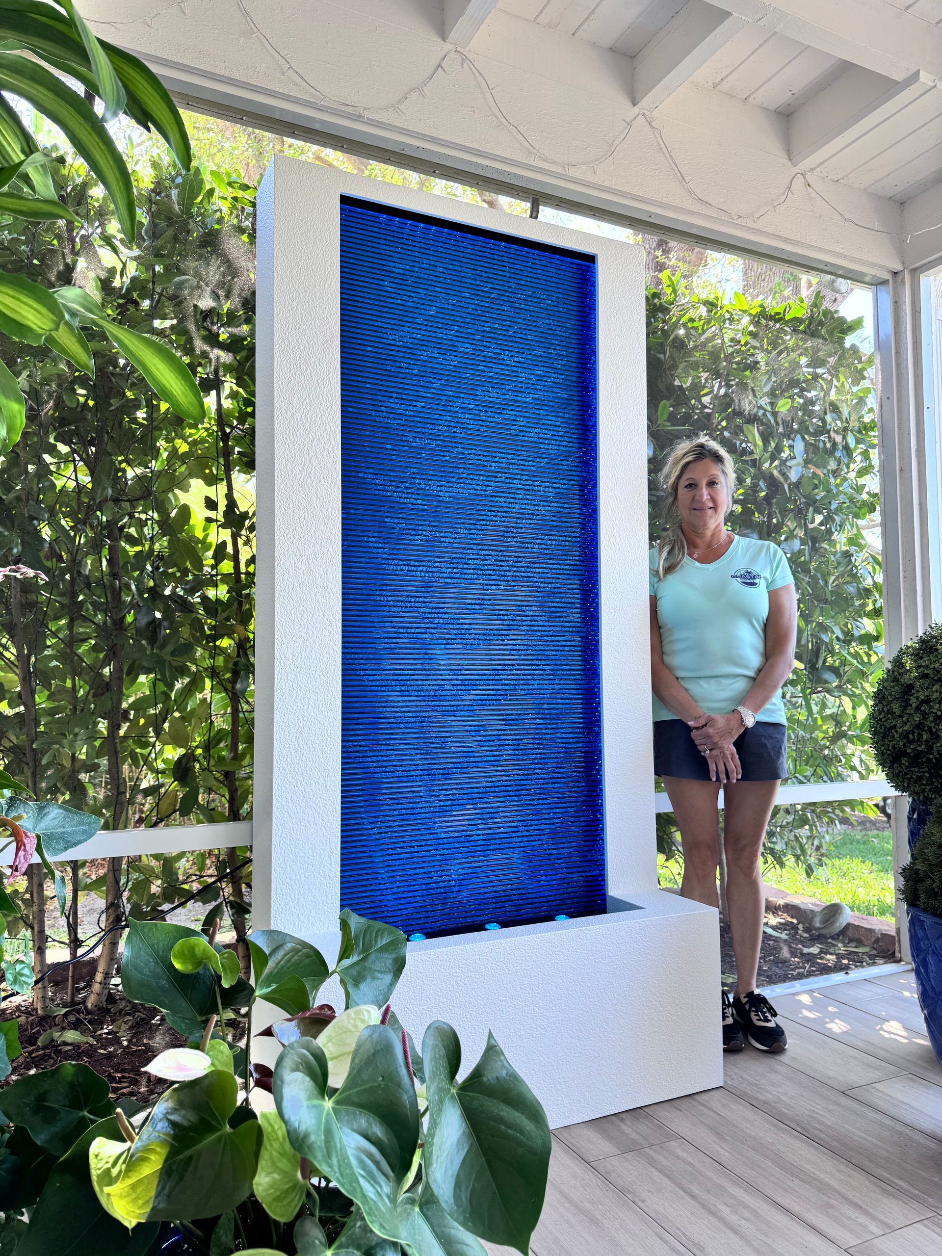 Woman stands beside a tall, blue glass water fountain on a porch