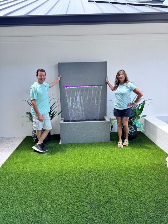 Couple beside a gray stone water fountain on green turf