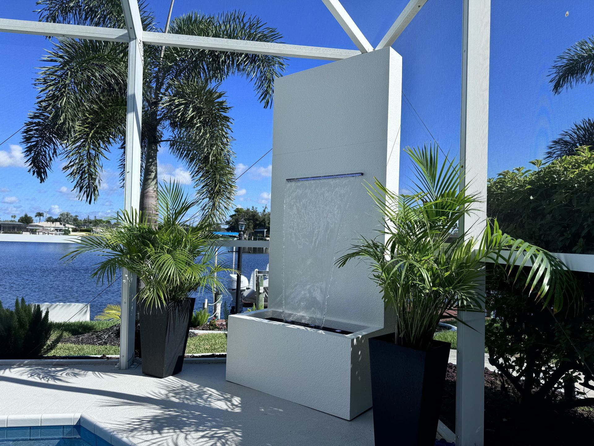 Modern outdoor water fountain with cascading water, flanked by potted plants