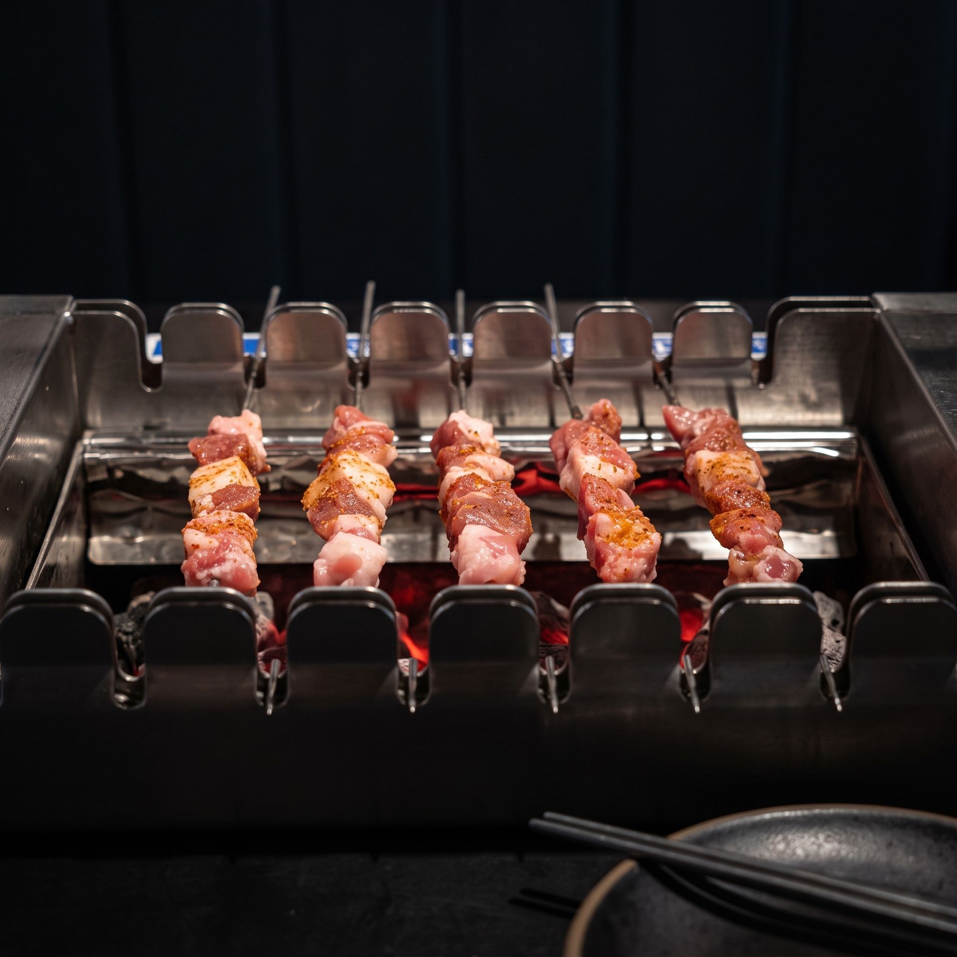 Skewers of grilled meat cooking on a metal tabletop barbecue rack with glowing coals below