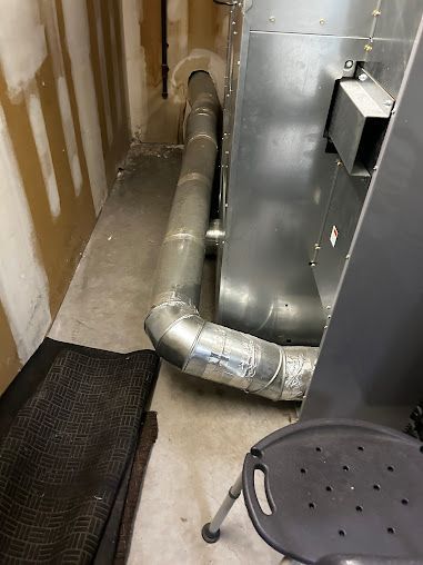 A metal pipe is going through a wall in a room next to a chair.