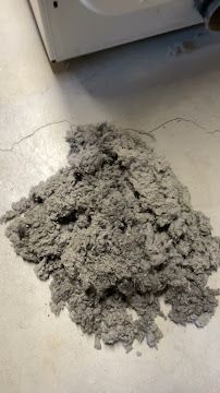 A pile of dust is sitting on the floor next to a washing machine.