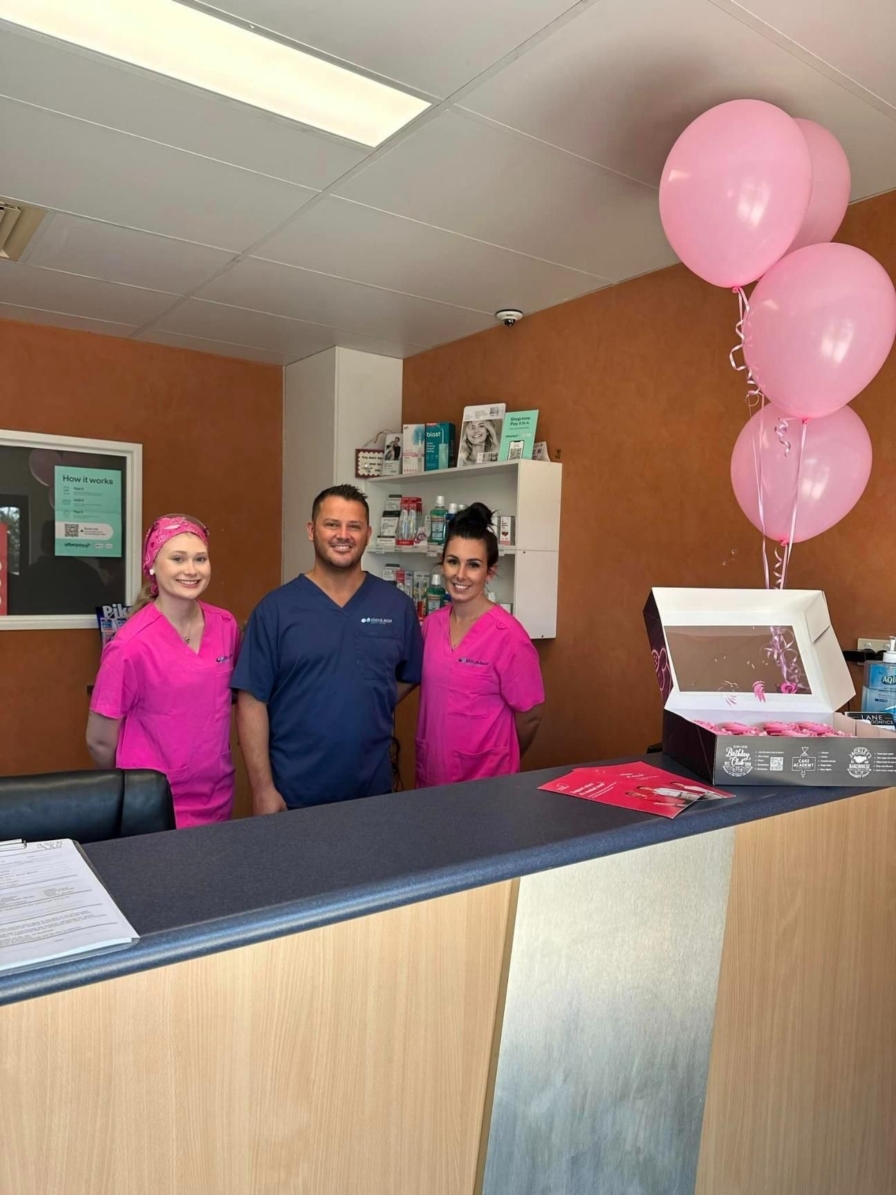 A group of people standing in front of a counter with pink balloons