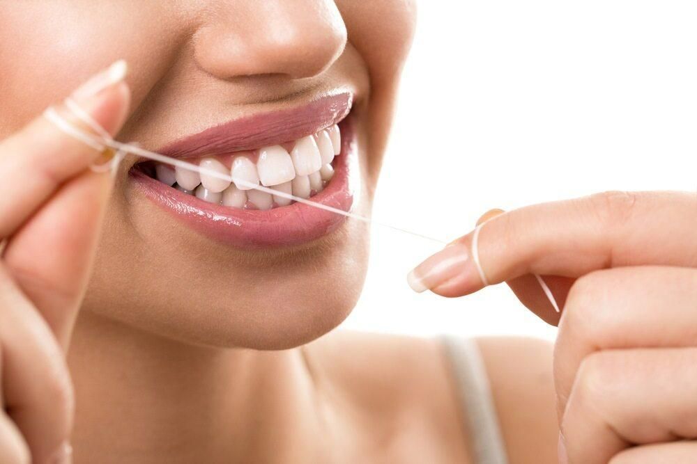 A Woman Is Flossing Her Teeth with A Dental Floss — Steve King Dental Group in Manunda, QLD