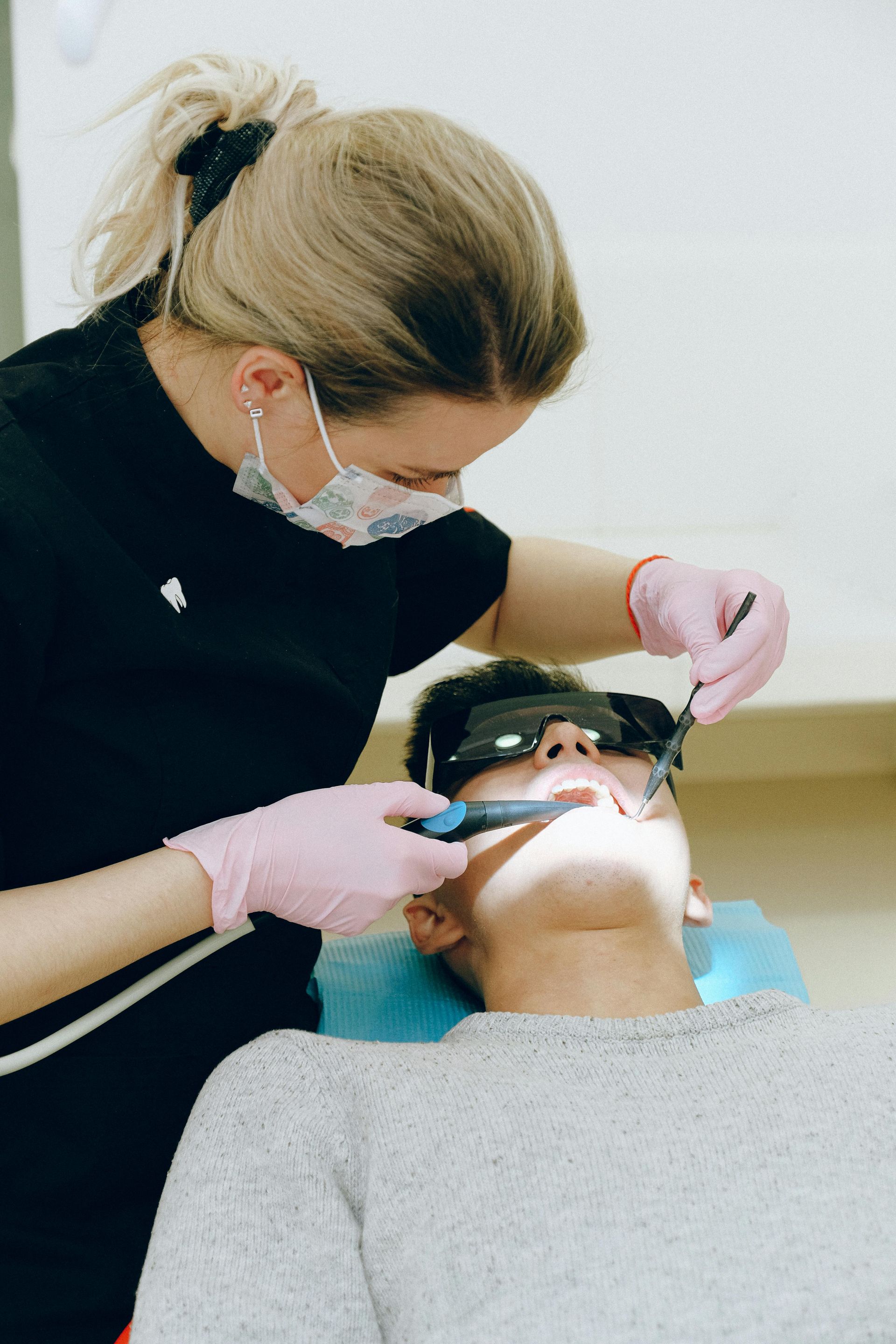 Dentist in mask and gloves working on patient's teeth. Patient wearing eye protection, in dental chair.— Steve King Dental Group in Manunda, QLD