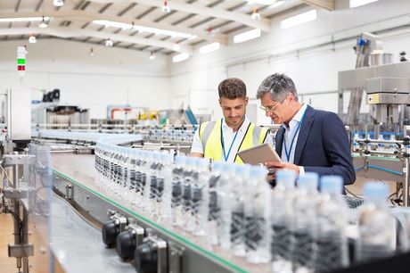 Two men inspecting bottles on a production line in a bright factory floor
