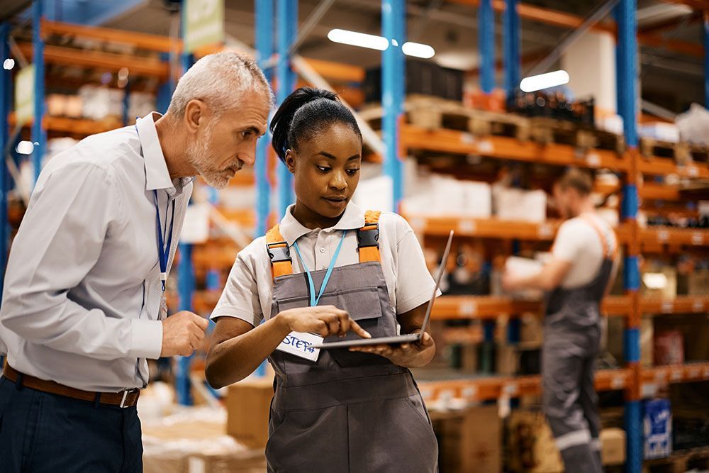 Two warehouse workers reviewing a tablet in an industrial storage aisle