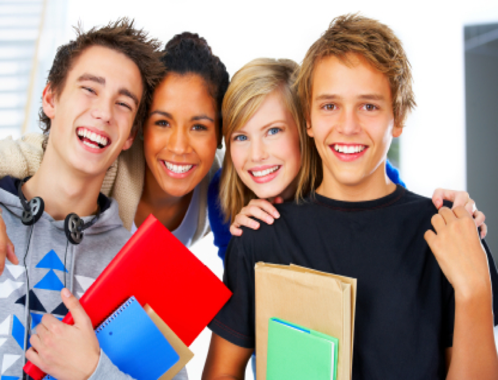 Four smiling students holding colorful notebooks in a classroom setting