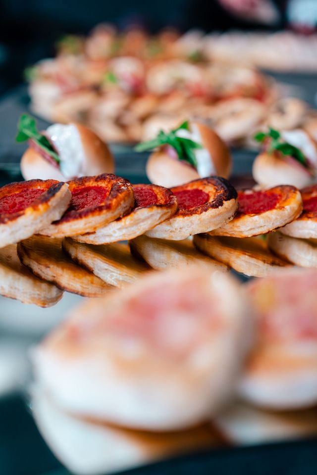 Antipasti assortiti in formato mini su cracker, guarniti con formaggio, erbe aromatiche e gamberetti, disposti su un piatto.